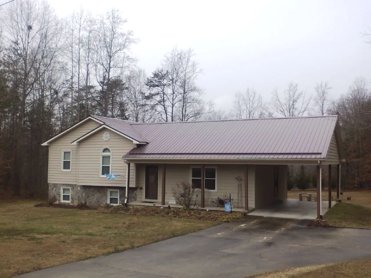 Burgundy metal roof on a tan split level home with an attached carport in Opelousas