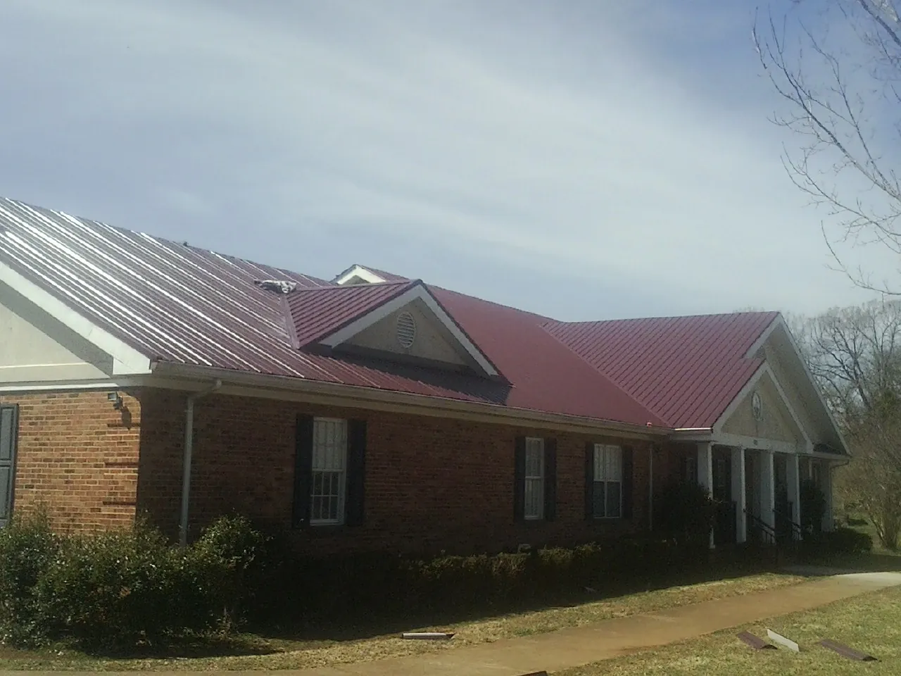 Red metal roof with gabled entries on a long brick building, from a Hail Damage Roof Repair job in Opelousas