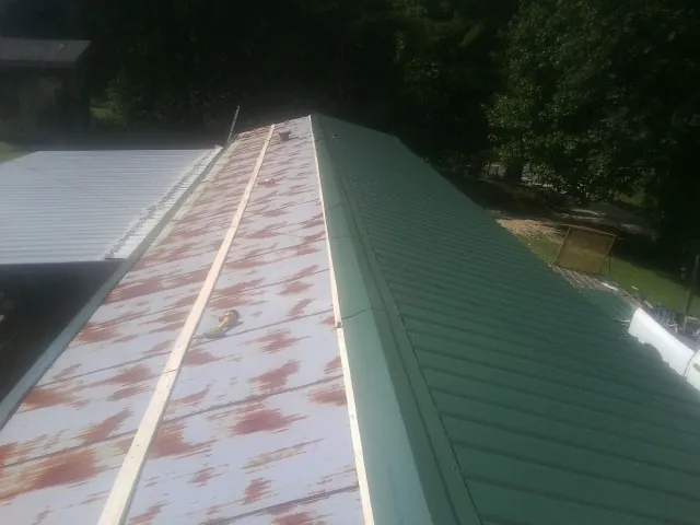 Old rusted panels beside newly installed green metal roofing — Wind Damage Roof Repair by Roofing Brothers in Opelousas