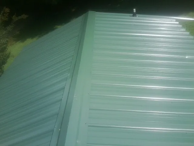 New green metal panels meeting at the ridge of a roof — Flat Roof Repair work by our crew in Opelousas