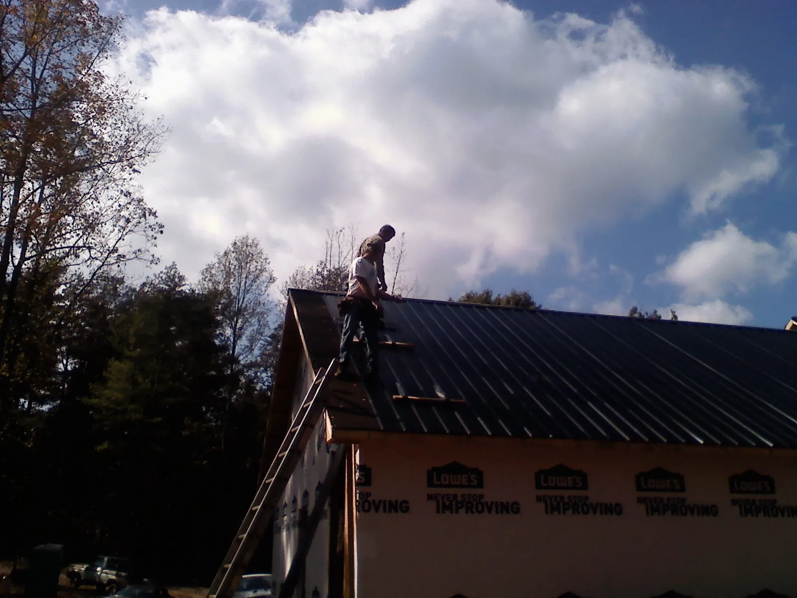 Roofer fastening dark metal panels high against a cloudy sky, from a Roof Inspection job in Opelousas