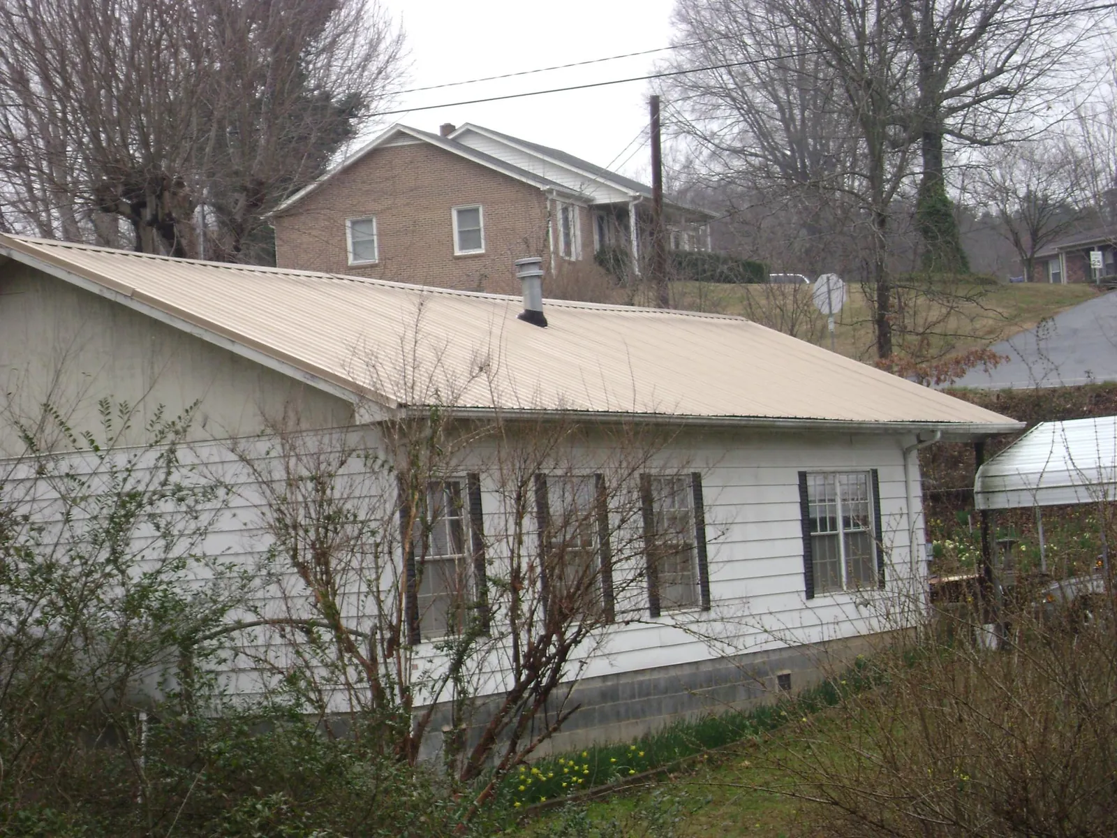 Tan metal roof on a white sided house set into a hillside — Commercial Roofing by Roofing Brothers in Opelousas