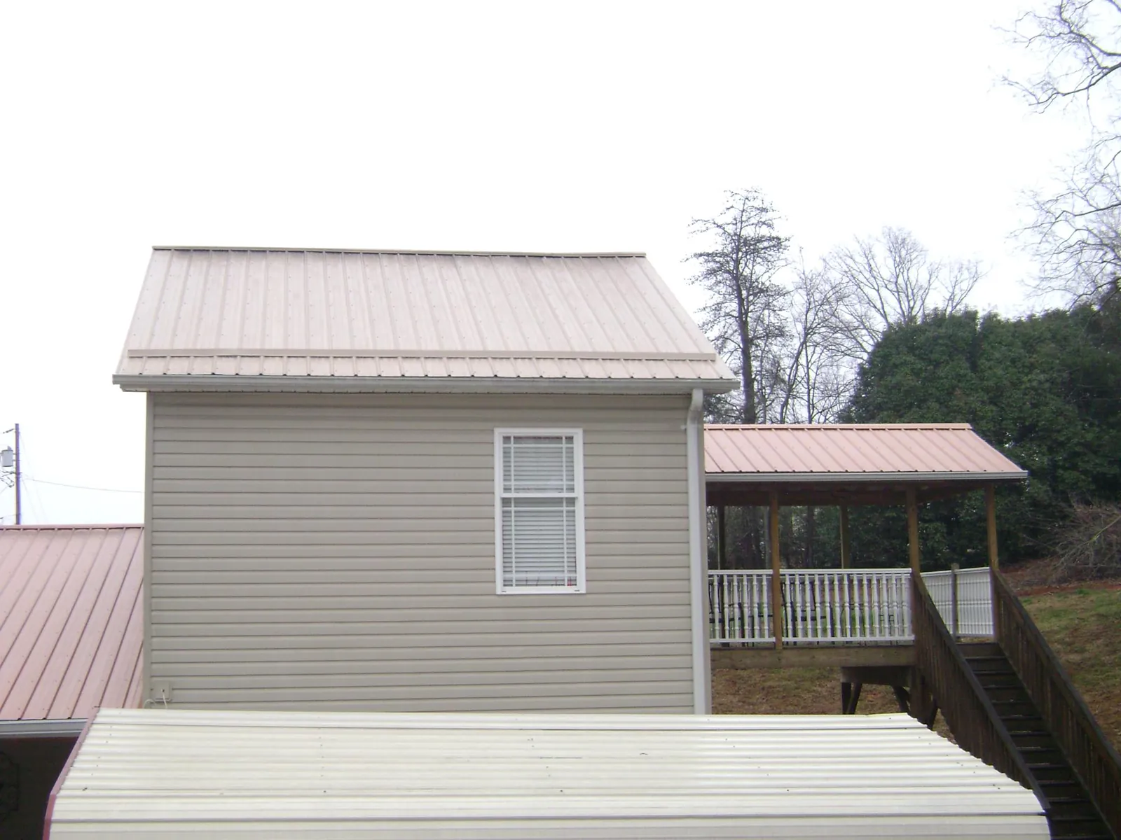 Tan metal roofs on a two story addition and attached porch, from a Roof Replacement job in Opelousas